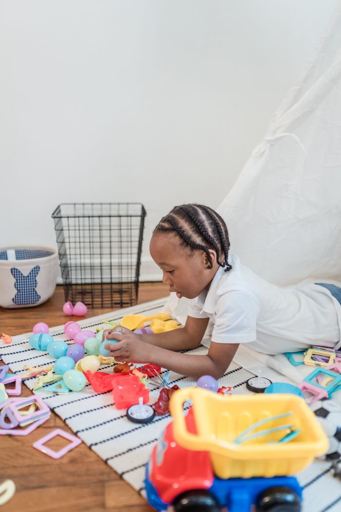 Services Joyful child playing with colorful toys indoors on a striped rug, expressing happiness and creativity.