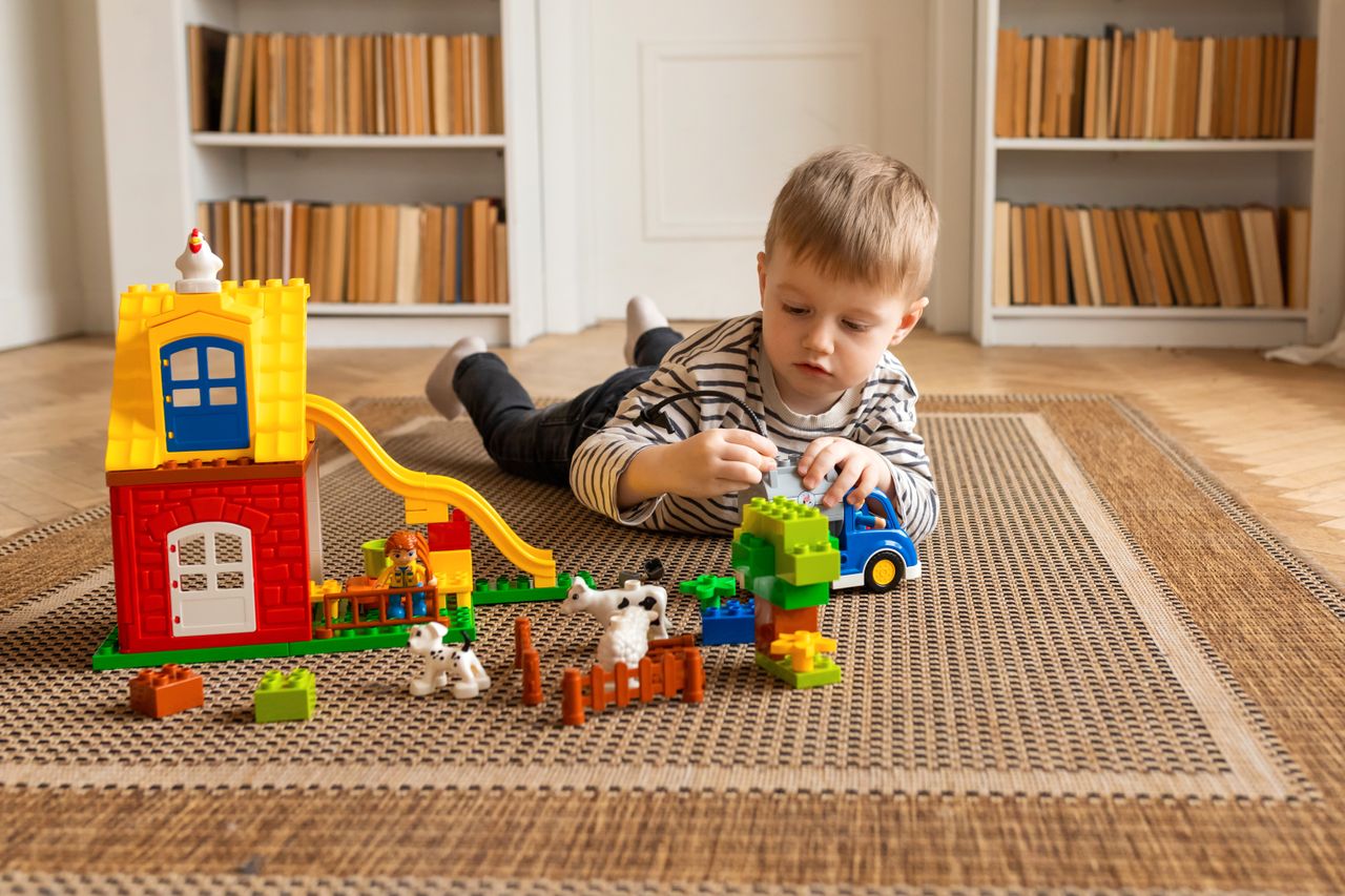 Young boy engaged in imaginative block play on a carpeted floor indoors.