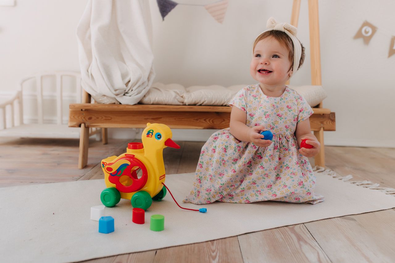 Services A smiling baby girl plays with a colorful toy in a cozy nursery setting.
