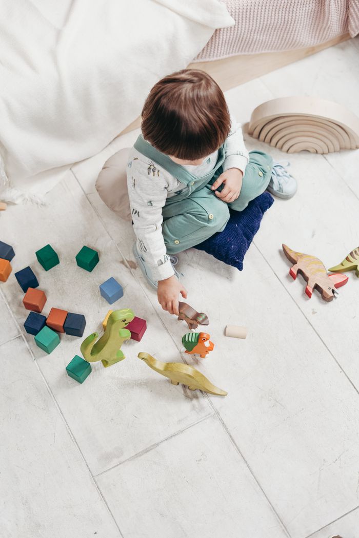 Services A young child engaged in play with colorful wooden toys on a tiled floor indoors.